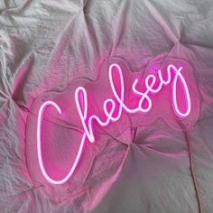 a pink neon sign that says cheers on top of a bed covered in white sheets