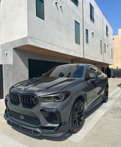 a grey bmw x4 parked in front of a building with two garage doors open