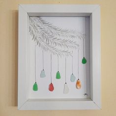 a white frame with christmas ornaments hanging from it's sides and on the wall