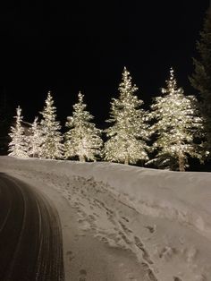 a snow covered road with trees and lights in the background