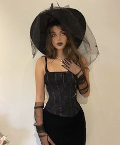 a woman in a black corset and hat poses for the camera with her hands on her hips