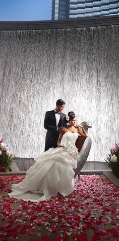 a bride and groom standing in front of a waterfall with rose petals on the ground