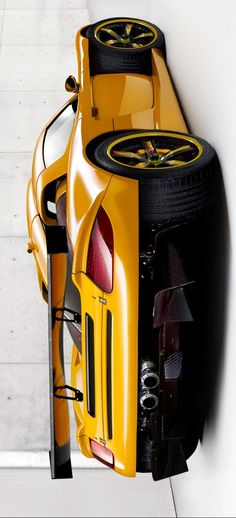 the rear end of a yellow sports car parked in a parking lot next to a white wall