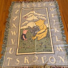 a winnie the pooh blanket with letters and animals on it, sitting on a wooden floor