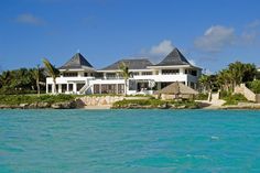 a large white house sitting on top of a lush green field next to the ocean