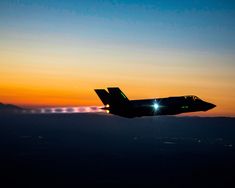 a fighter jet flying through the air at sunset