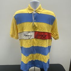 This Vintage Tommy Hilfiger Polo Shirt Is A Must-Have For Any Fashion-Savvy Man. With A Unique Spellout Striped Colorblock Design, This Shirt Is Perfect For Casual Occasions And Can Be Worn In All Seasons. The Shirt Is Made Of 100% Cotton Knit Fabric, Which Ensures Both Comfort And Durability. Featuring A Collared Neckline With A Point Collar Style And Short Sleeves, This Classic Fit Shirt Has A Button Closure And Accent Buttons. The Shirt Is Machine Washable And Has A Size Of Medium. It Is A Pe Fitted Cotton Shirt With Color Block, Fitted Cotton Color Block Shirt, Tommy Hilfiger Striped Tops For Summer, Summer Striped Tops By Tommy Hilfiger, Tommy Hilfiger Yellow Cotton Tops, Yellow Cotton Tommy Hilfiger Top, Yellow Tommy Hilfiger Cotton Top, Fitted Casual Color Block Shirt, Sporty Fitted Tommy Hilfiger Tops