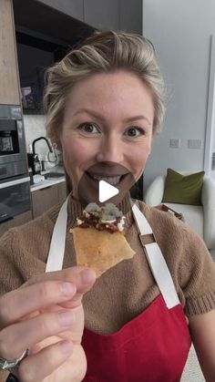 a woman in an apron is holding up a piece of food to her mouth and smiling