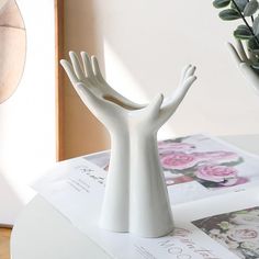 a white hand statue sitting on top of a table next to a potted plant