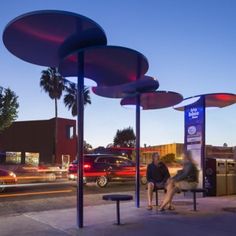 two people are sitting on a bench in front of a bus stop at night time