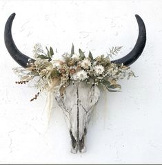 an animal skull with flowers on it's head against a white wall and cement background