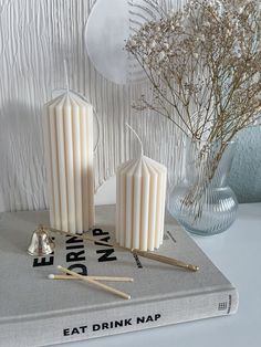 two candles on top of a book next to a vase with dried flowers in it