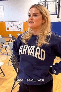 a woman standing in a gym with her hands on her hips and looking off to the side