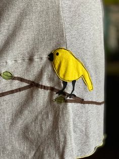 a yellow bird sitting on top of a tree branch next to a person's shirt