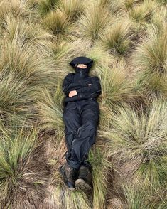 a man is laying in the grass wearing a black jacket and hat with his eyes closed