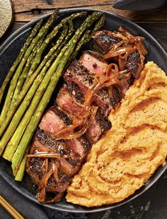 steak, mashed potatoes and asparagus in a pan on a wooden table