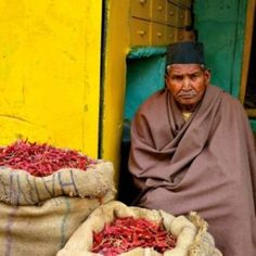 a man sitting in front of two bags of dried red chilis on the ground