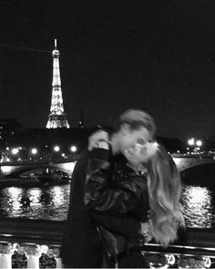 a man and woman kissing in front of the eiffel tower at night, paris