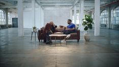 two women sitting on couches in an industrial building, one is talking to the other