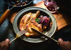 a plate with meat and vegetables on it next to a person holding a knife and fork