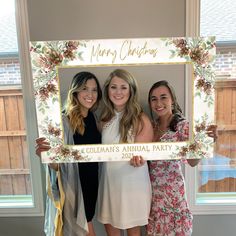 three women pose for a photo in front of a floral frame with the word bridal shower written on it