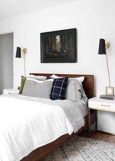 a bed with white sheets and pillows in a bedroom next to a painting on the wall