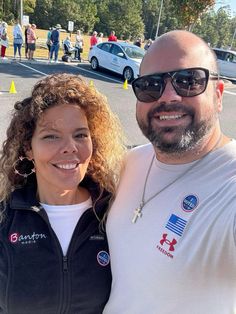 a man and woman standing next to each other in front of a parking lot full of cars