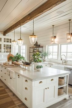 a large white kitchen with lots of counter space and lights hanging from the ceiling above it