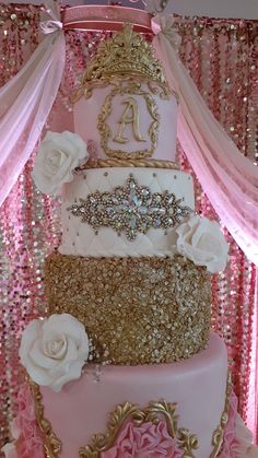 a pink and gold wedding cake with roses on the bottom, surrounded by sequins