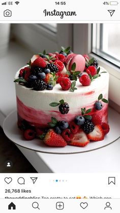 a cake decorated with berries and strawberries on top of a white plate next to a window