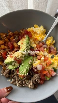 a person holding a white bowl filled with eggs, meat and vegtables