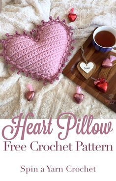 a crochet heart pillow sitting on top of a bed next to a cup of coffee