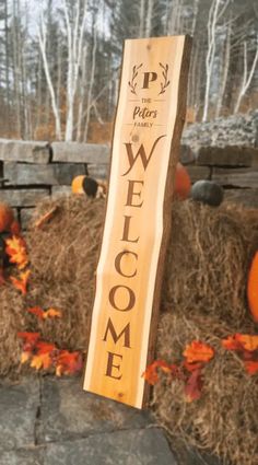 a welcome sign in front of hay bales with pumpkins on the ground behind it