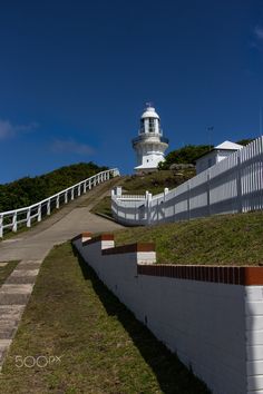 a white lighthouse on top of a hill next to a walkway and fenced in area