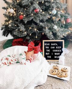 a baby is laying in front of a christmas tree with cookies on the floor and a sign that says dear santa, you can keep the cookies but i want the milk