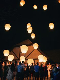 many people are standing around with paper lanterns in the air above them, all lit up at night