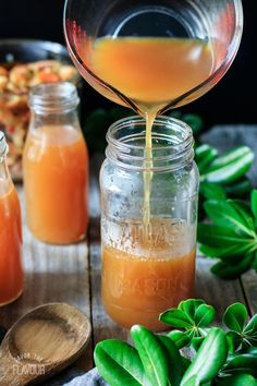 an orange liquid being poured into a mason jar with leaves around it and other ingredients in the background