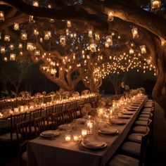 a long table with many lit candles under a tree filled with hanging lanterns and chairs