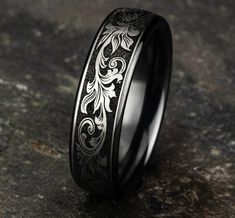 a black and white wedding ring with an intricate design on the inside, sitting on a stone surface