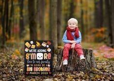 a young boy sitting on top of a tree stump in the woods next to a sign that says we're adding smore