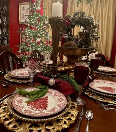 a dining room table set for christmas with plates, silverware and candlesticks