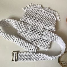 a white knitted object with a metal buckle on it's side next to a clock