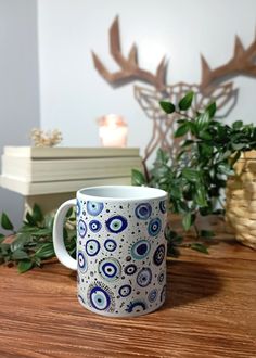 a blue and white coffee mug sitting on top of a wooden table next to a plant