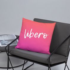 a pink pillow sitting on top of a black chair next to a table with a magazine