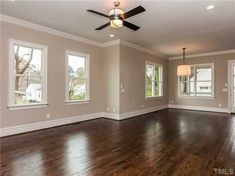 an empty living room with hard wood floors and ceiling fan in the center, two windows on both sides