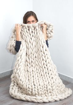 a woman is holding up a large chunky blanket