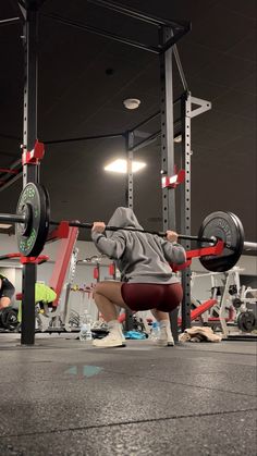 a man squats down while holding a barbell in front of his face as he works out at the gym