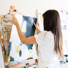 a woman is painting on an easel in her art studio while holding a brush