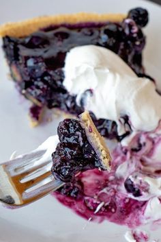 a slice of blueberry pie on a white plate with ice cream and a fork