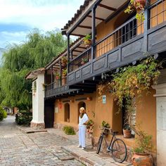 a woman standing in front of a building next to a bicycle and potted plants